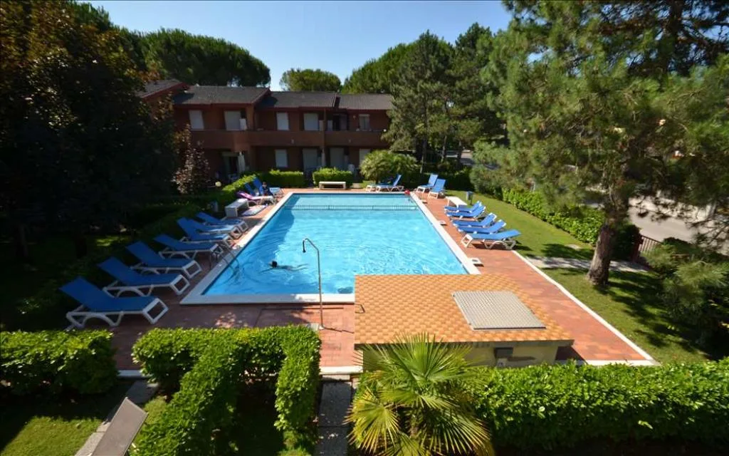 Veduta dall'alto della piscina con lettini blu circondata da giardino e pini